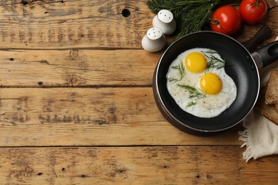 Frying pan with tasty cooked eggs, dill and other products on wooden table, flat lay. Space for text