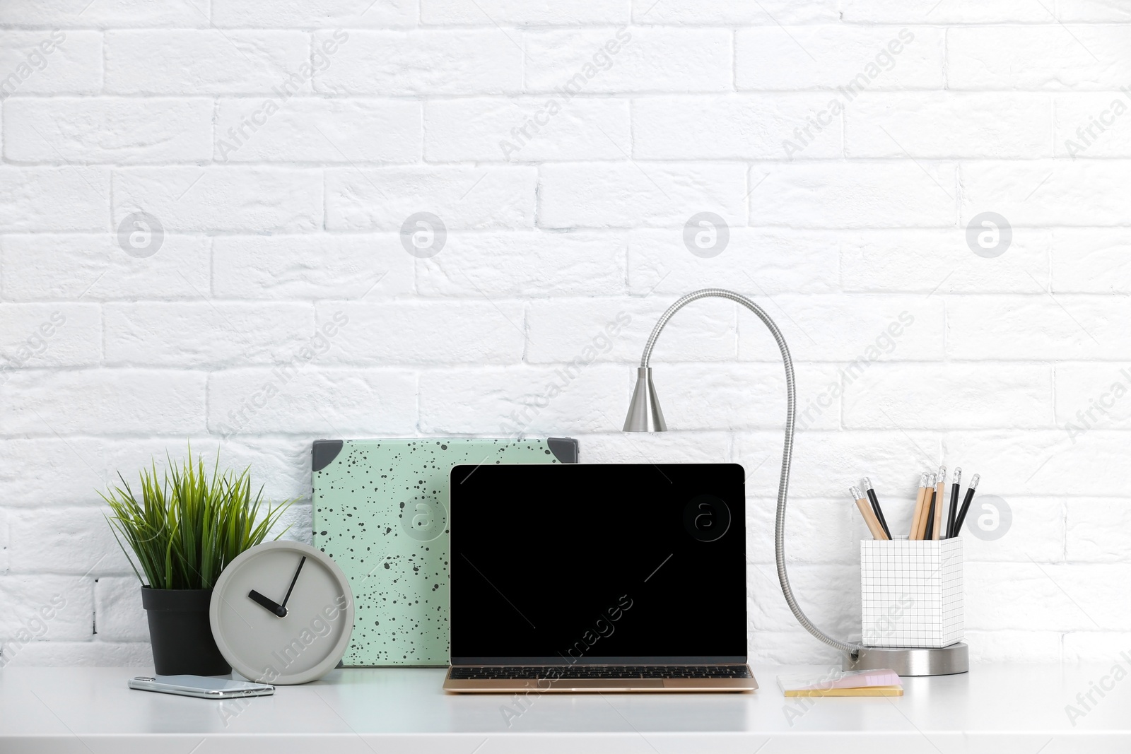 Photo of Modern workplace with laptop on table against brick wall. Mockup for design