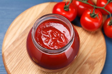 Photo of Organic ketchup in jar and fresh tomatoes on blue wooden table, closeup. Tomato sauce