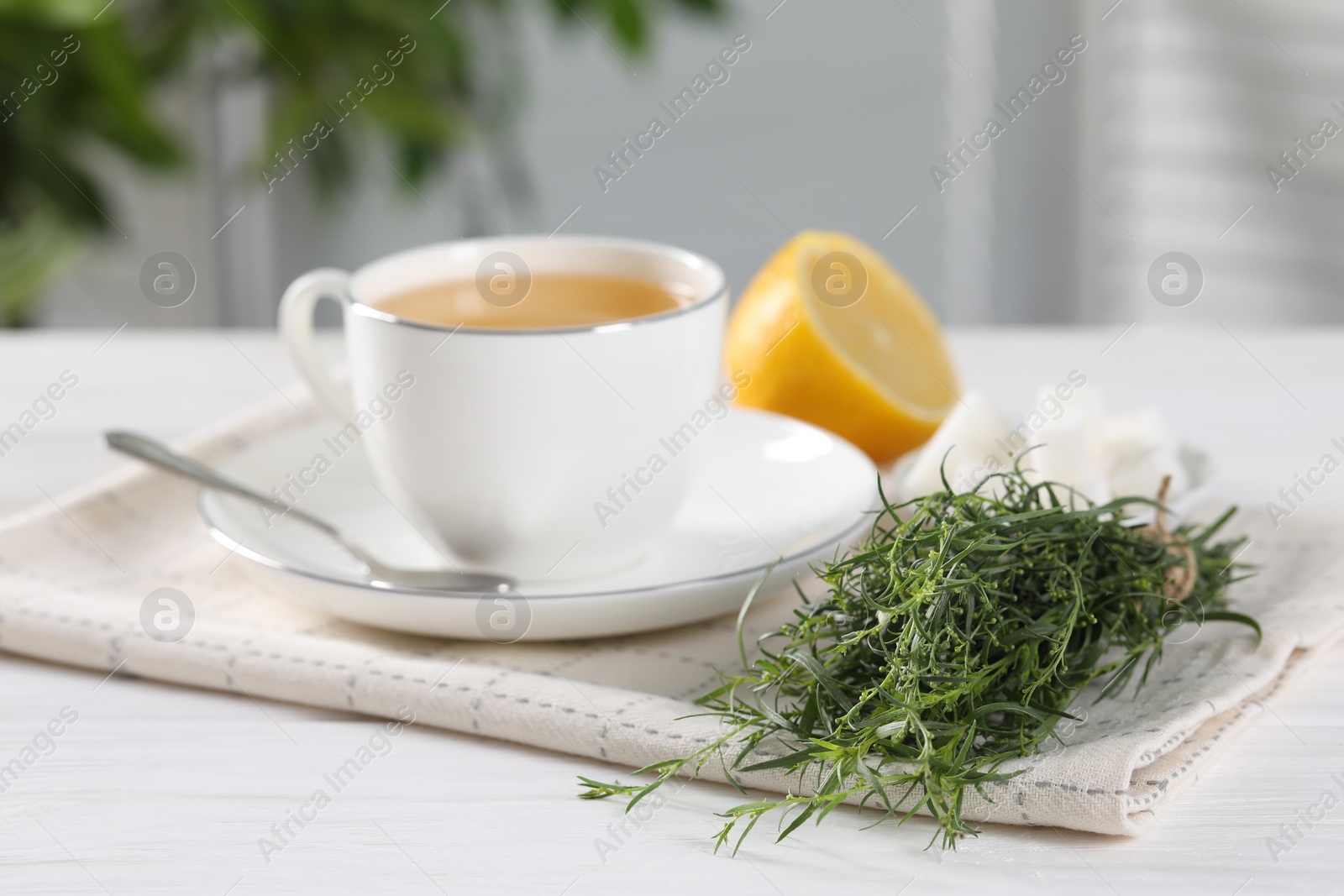 Photo of Aromatic herbal tea, fresh tarragon sprigs, sugar cubes and lemon on white wooden table