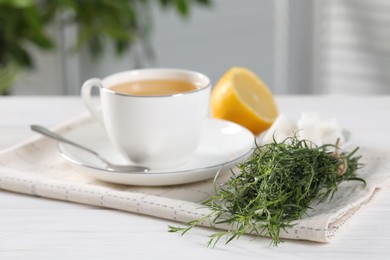 Aromatic herbal tea, fresh tarragon sprigs, sugar cubes and lemon on white wooden table