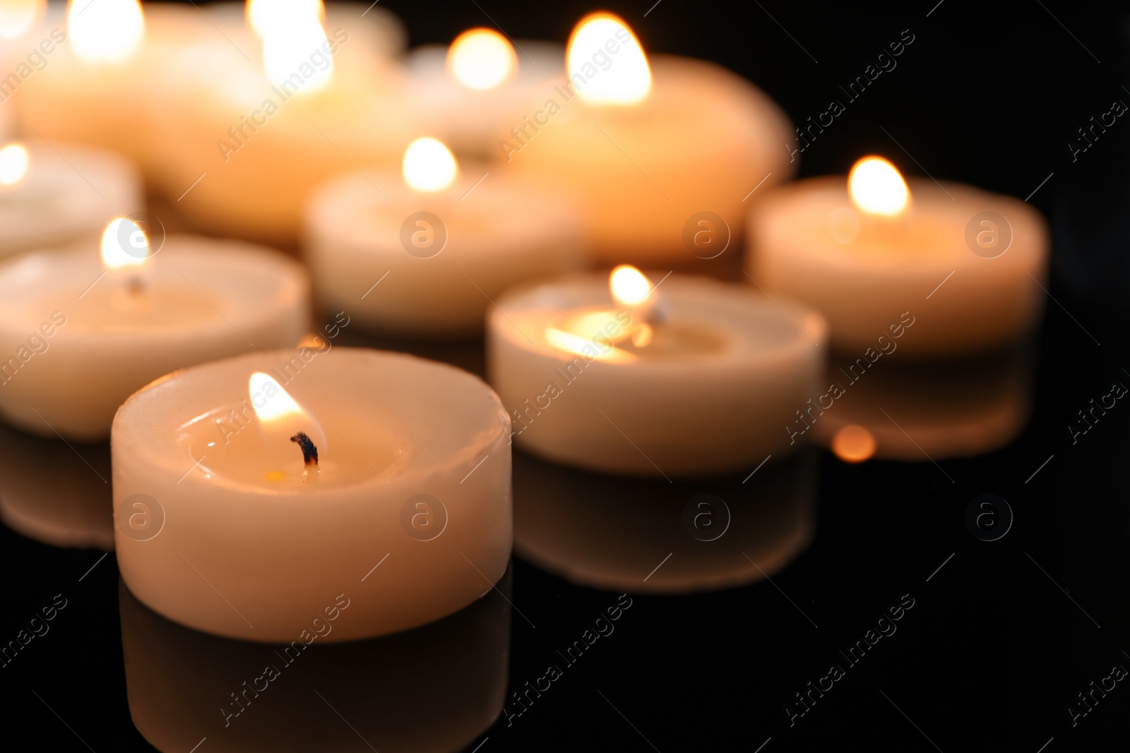 Photo of Wax candles burning on table in darkness, closeup