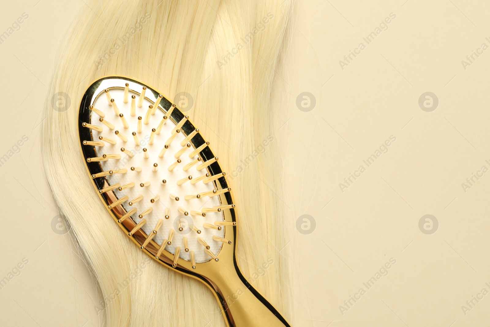 Photo of Stylish brush with blonde hair strand on beige background, top view. Space for text