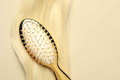 Stylish brush with blonde hair strand on beige background, top view. Space for text