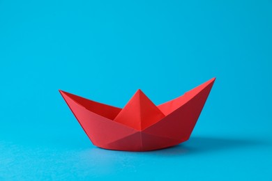 Handmade red paper boat on light blue background. Origami art