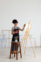 Young woman painting on easel with canvas in studio