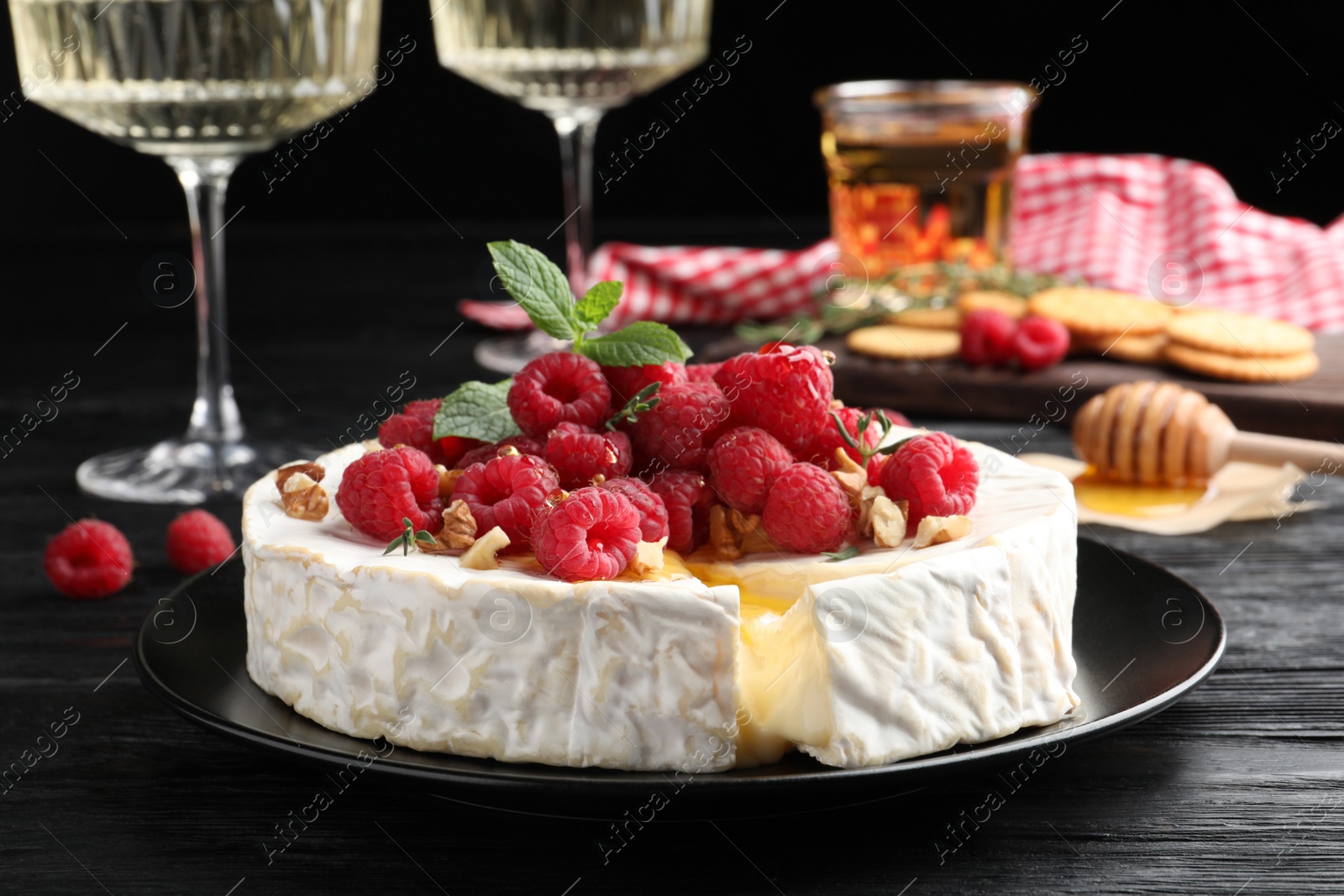 Photo of Brie cheese served with raspberries and walnuts on black wooden table