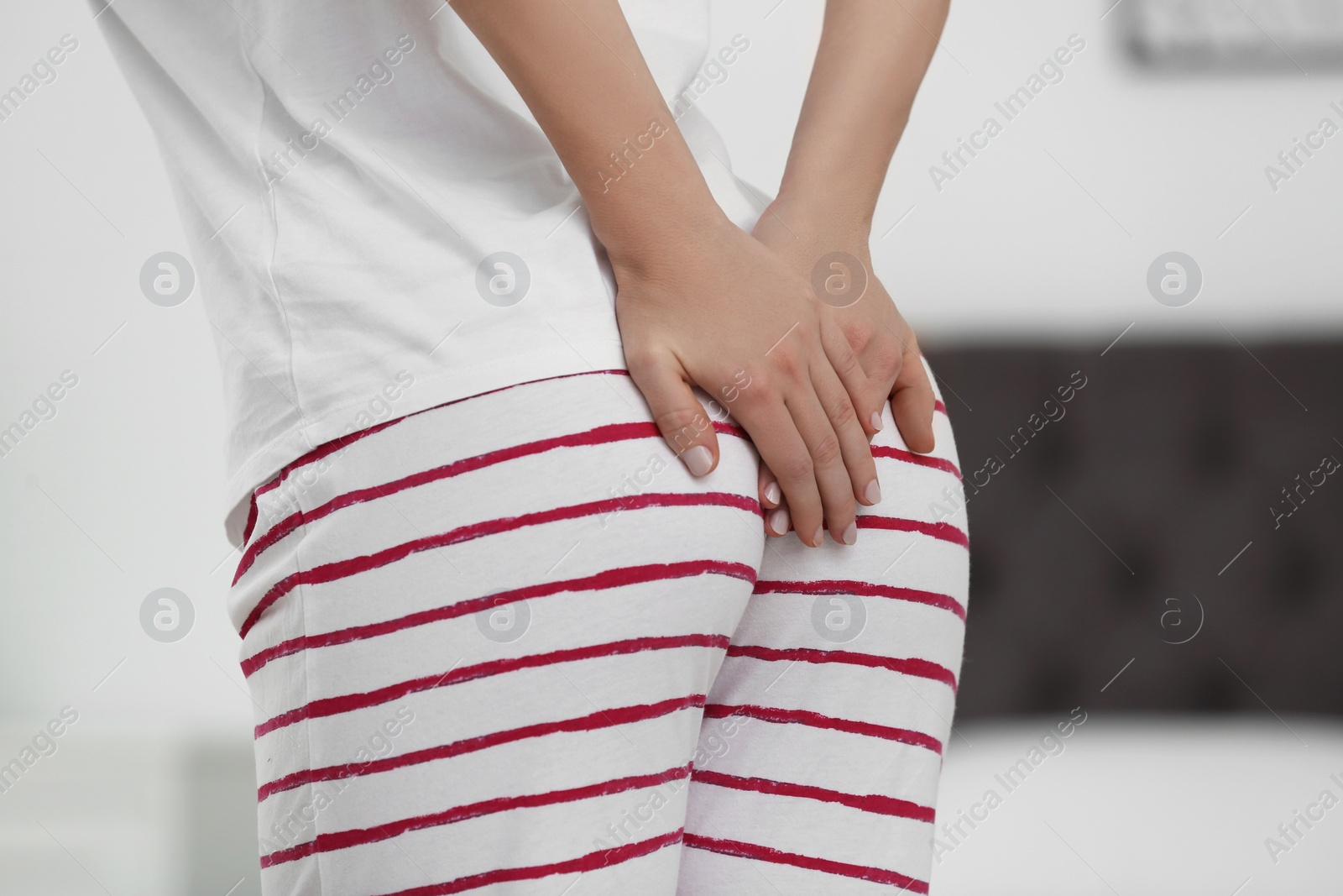 Photo of Young woman suffering from hemorrhoid in bedroom, closeup