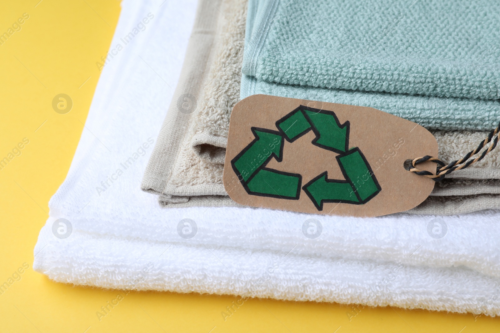 Photo of Stacked towels with recycling label on yellow background, closeup