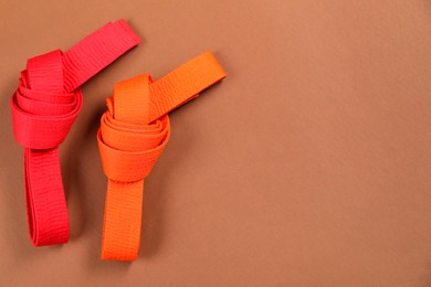 Colorful karate belts on brown background, flat lay. Space for text