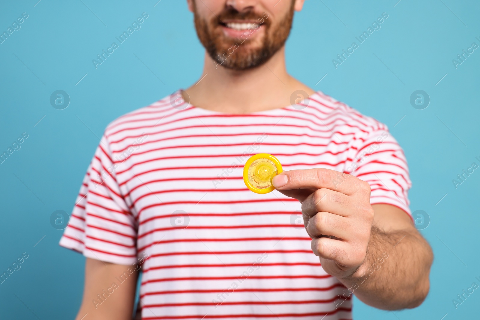 Photo of Man holding condom on light blue background, closeup. Safe sex