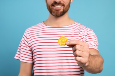 Photo of Man holding condom on light blue background, closeup. Safe sex