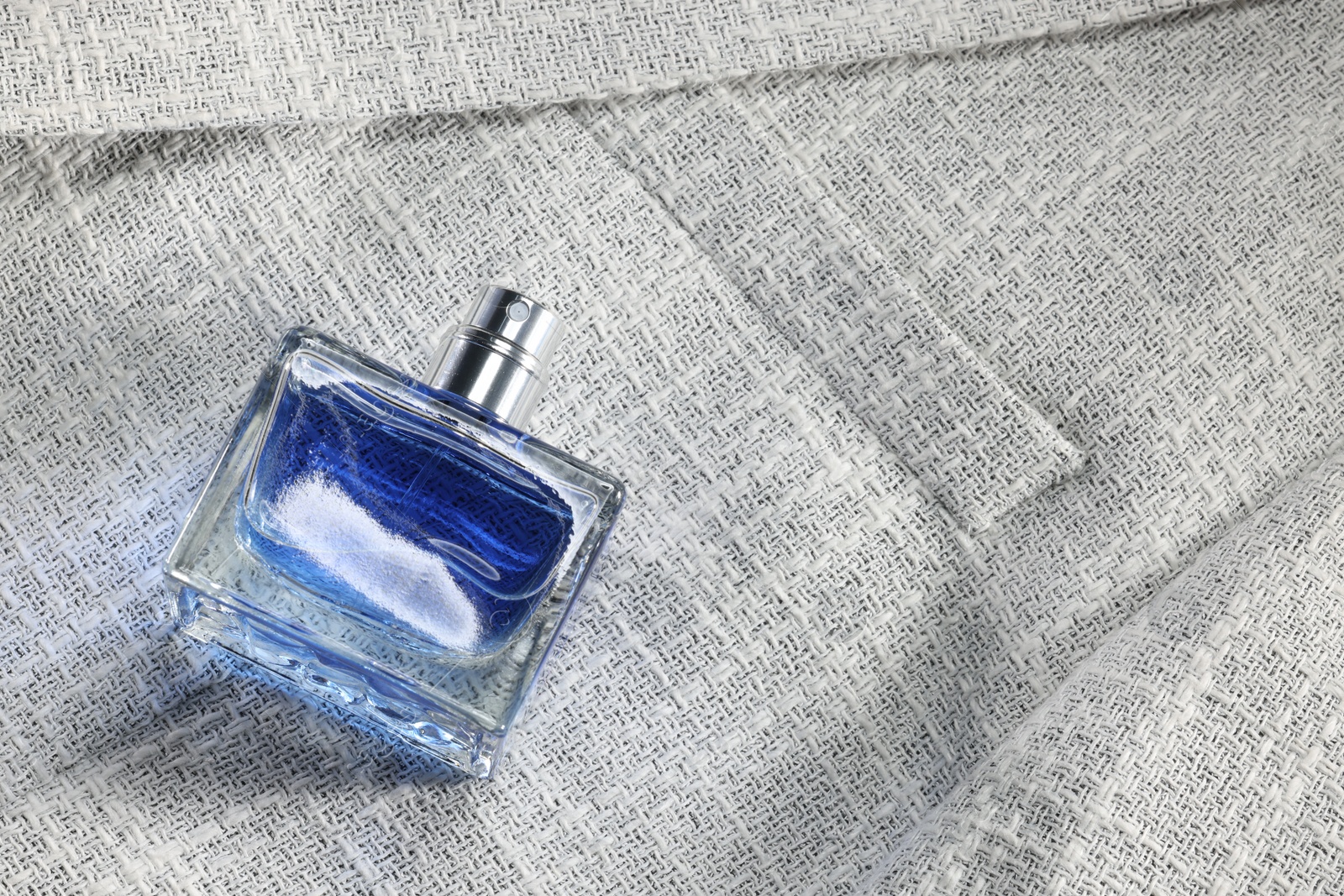 Photo of Luxury men's perfume in bottle on grey jacket, above view. Space for text