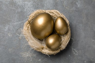 Golden eggs in nest on grey table, top view