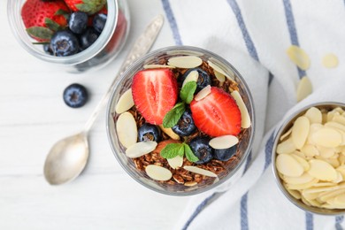 Photo of Tasty granola with berries, almond flakes and mint in glass on white table, flat lay