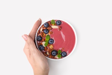 Woman holding bowl of delicious smoothie with fresh blueberries and granola on white background, top view