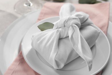Photo of Furoshiki technique. Gift packed in white fabric and eucalyptus leaf on table, closeup