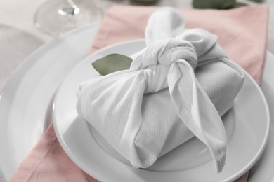 Furoshiki technique. Gift packed in white fabric and eucalyptus leaf on table, closeup