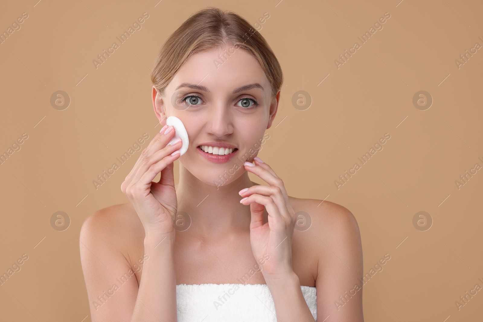 Photo of Young woman cleaning her face with cotton pad on beige background