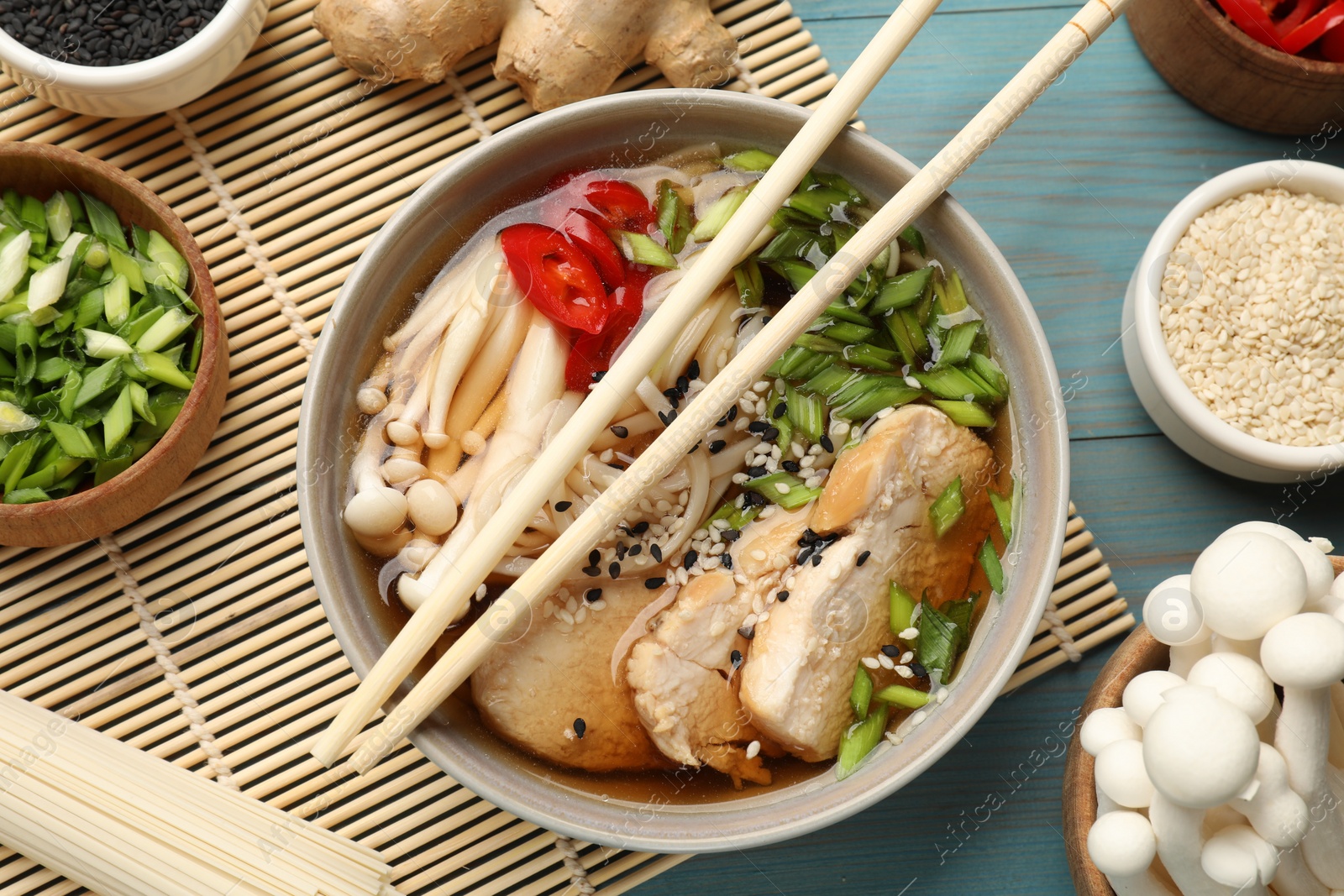 Photo of Delicious ramen with meat and ingredients on light blue wooden table, flat lay. Noodle soup