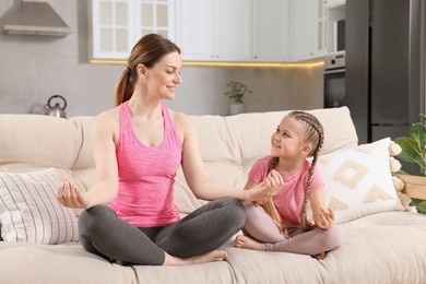 Photo of Mother with daughter meditating on sofa at home