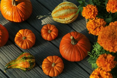 Photo of Many whole ripe pumpkins and potted marigold flowers on wooden table