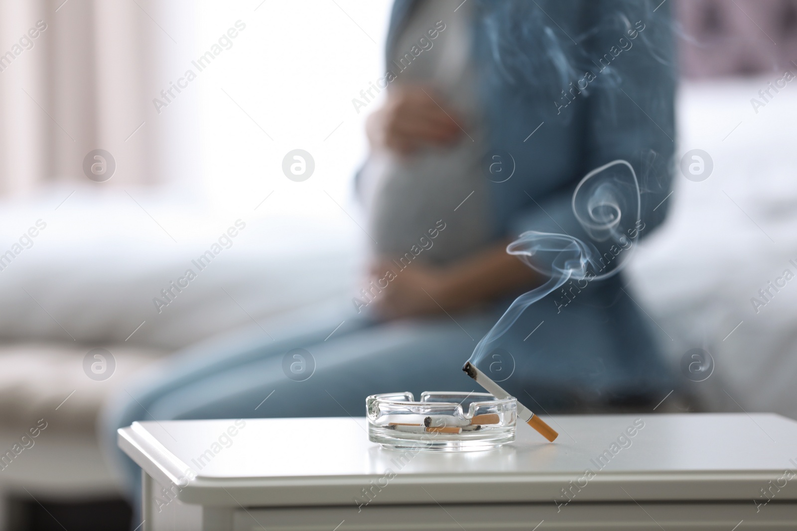 Photo of Cigarettes in ash tray and blurred pregnant woman on background, closeup. Space for text