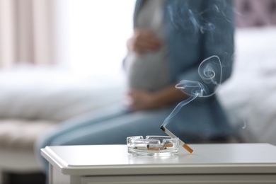 Cigarettes in ash tray and blurred pregnant woman on background, closeup. Space for text