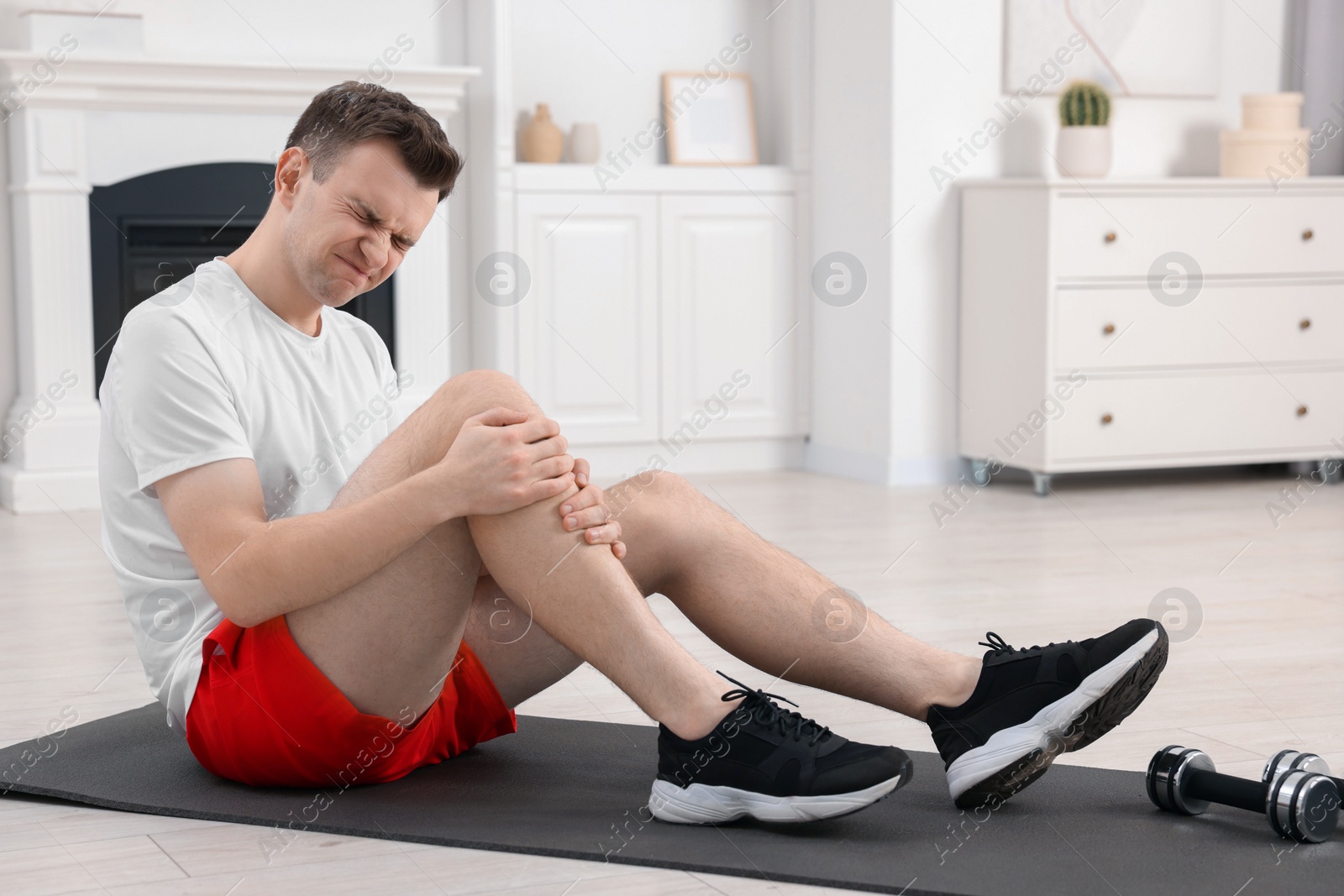 Photo of Man suffering from leg pain on mat at home