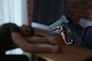 Photo of Man with gun and his victim in room, closeup. Dangerous criminal