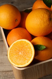 Photo of Many whole and cut ripe oranges on wooden table, closeup