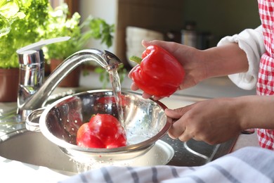 Photo of Woman washing fresh bell peppers in kitchen sink, closeup