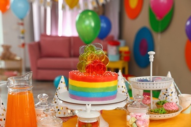 Photo of Bright birthday cake and other treats on table in decorated room