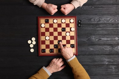 Photo of Senior man playing checkers with angry partner at black wooden table, top view