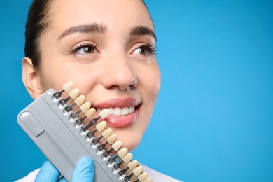 Photo of Doctor checking young woman's teeth color on blue background, closeup. Cosmetic dentistry