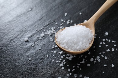 Photo of Organic white salt and spoon on black table, closeup. Space for text