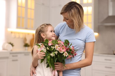 Photo of Little daughter congratulating her mom with bouquet of alstroemeria flowers in kitchen. Happy Mother's Day