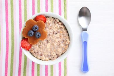 Photo of Tasty porridge served with berries on white wooden table, flat lay. Creative idea for kids breakfast