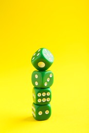 Photo of Many stacked green game dices on yellow background, closeup