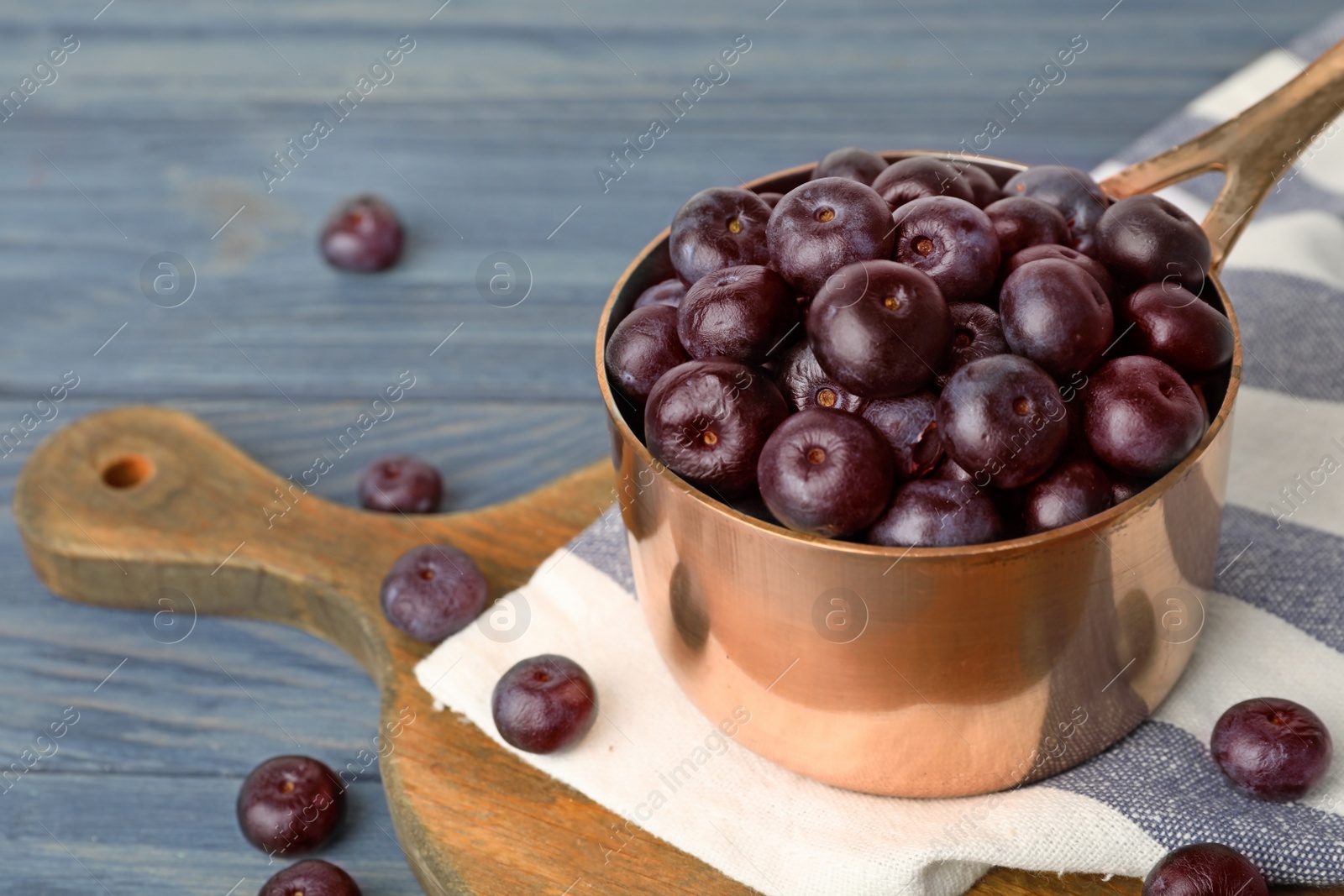 Photo of Metal saucepan of fresh acai berries on blue wooden table, space for text