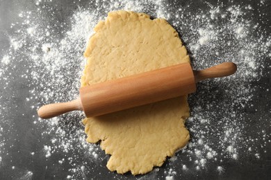 Photo of Making shortcrust pastry. Raw dough, flour and rolling pin on grey table, top view