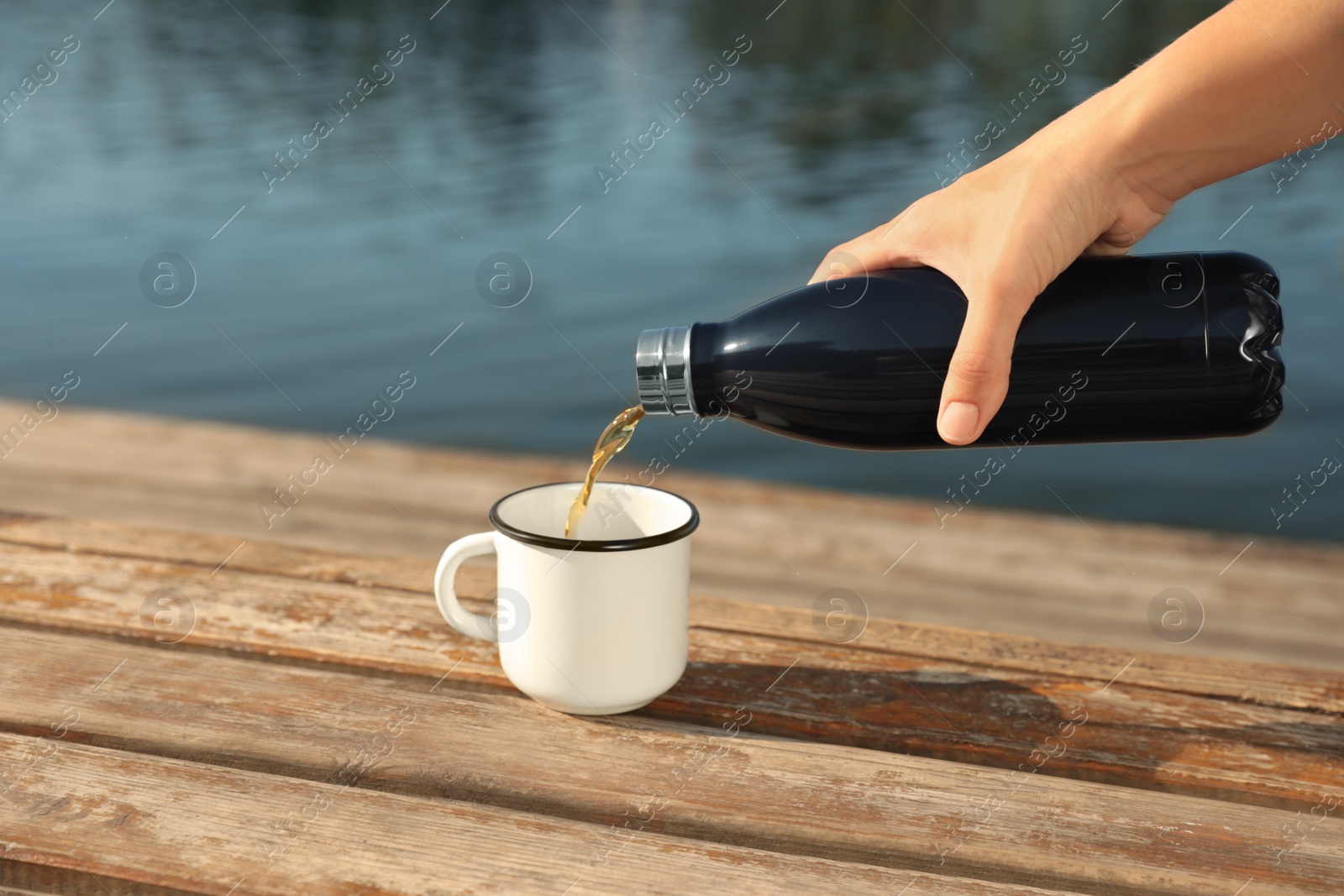 Photo of Woman pouring hot drink from thermos bottle into cup outdoors, closeup