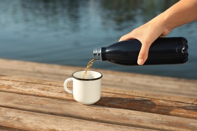 Woman pouring hot drink from thermos bottle into cup outdoors, closeup