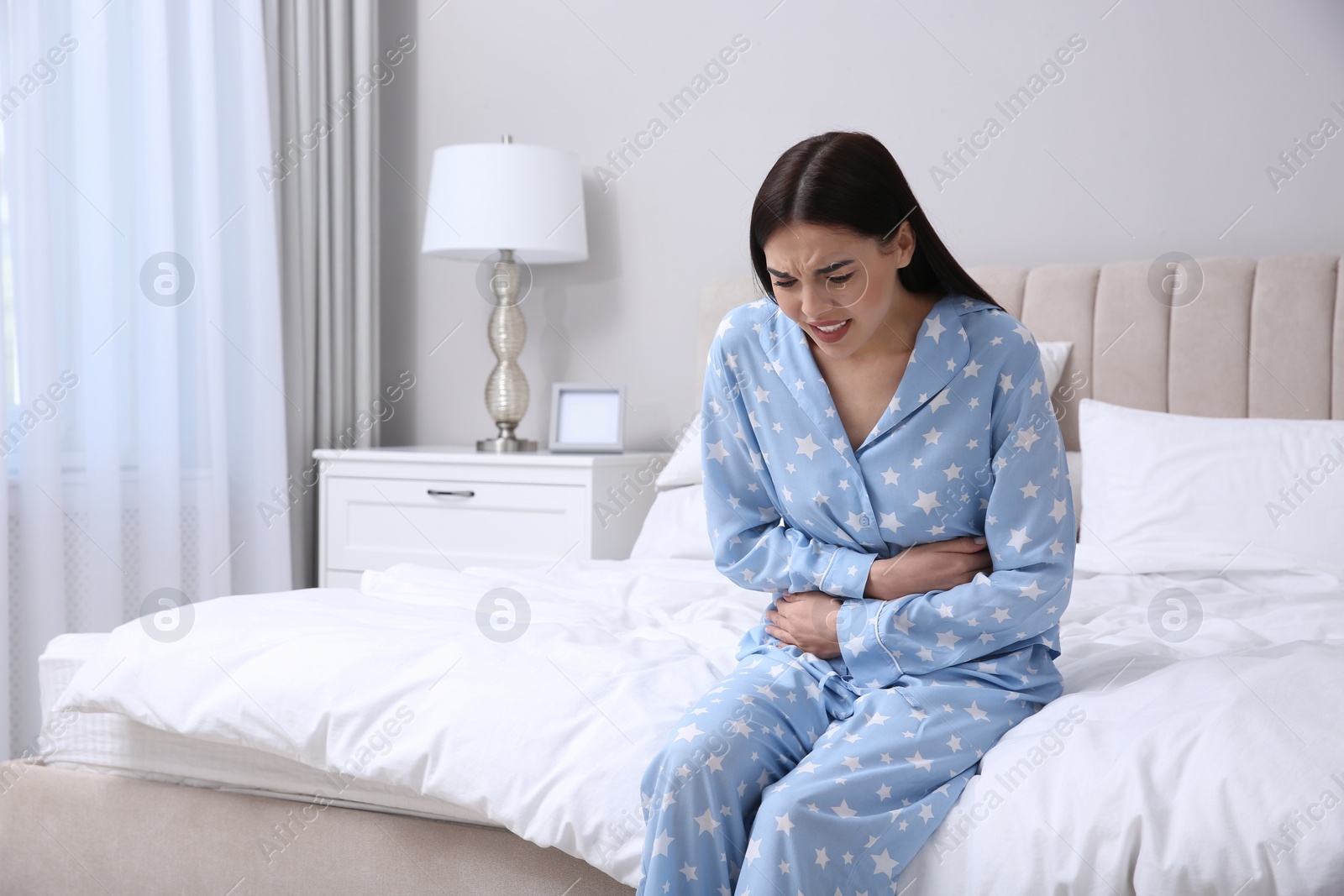 Photo of Young woman suffering from stomach ache in bedroom