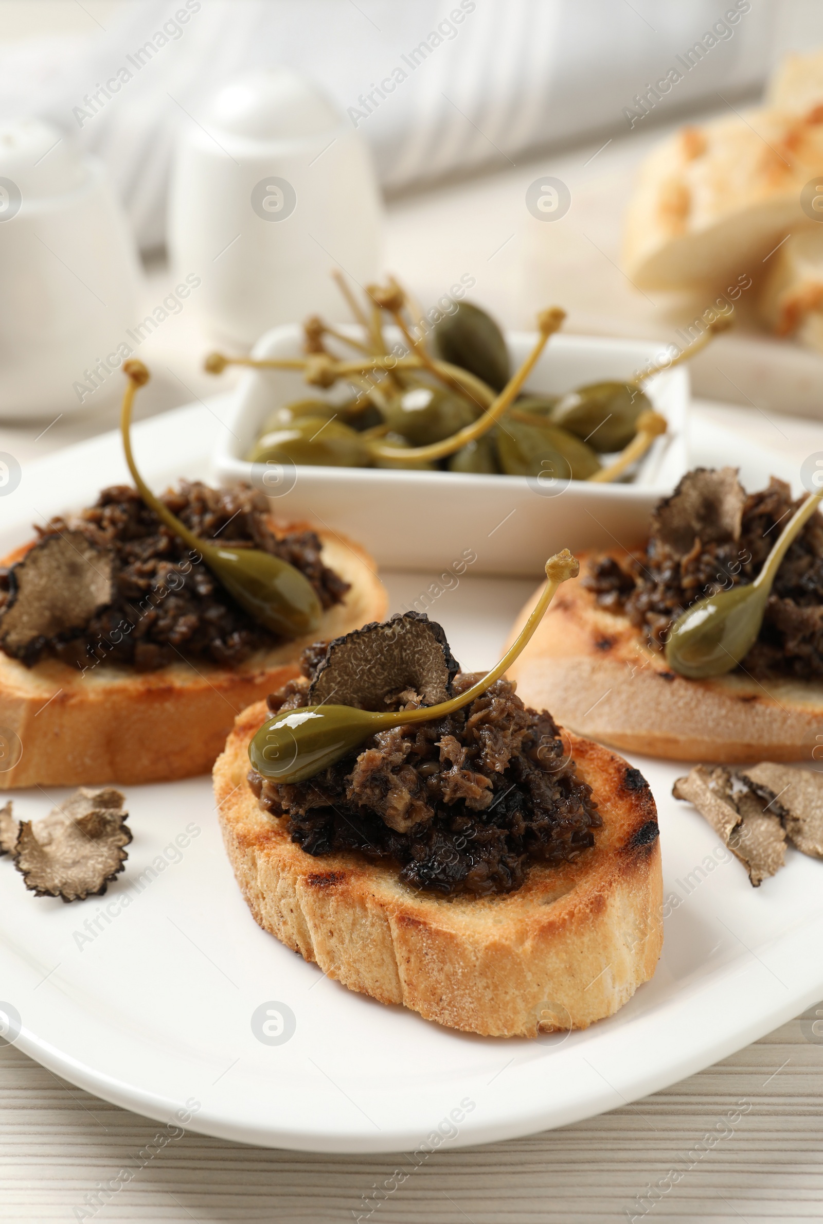 Photo of Delicious bruschettas with truffle sauce and caperberries on white wooden table, closeup