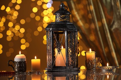 Photo of Arabic lantern and burning candles on mirror surface against blurred lights