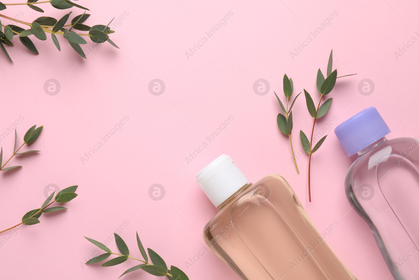 Photo of Bottles of baby oils and green leaves on pink background, flat lay. Space for text