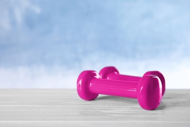 Photo of Stylish dumbbells on table against color background, space for text. Fitness equipment