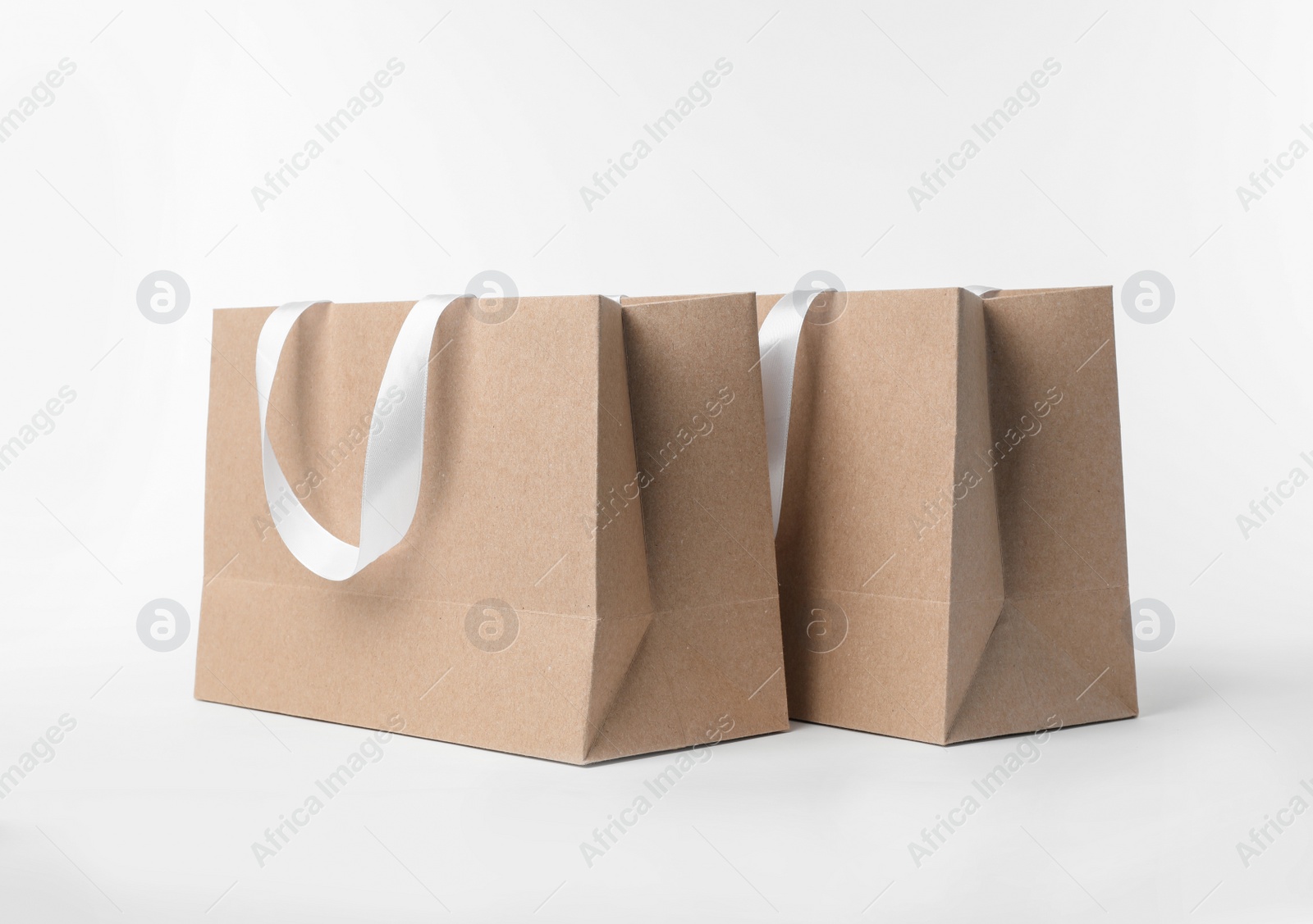 Photo of Paper shopping bags with ribbon handles on white background. Mockup for design