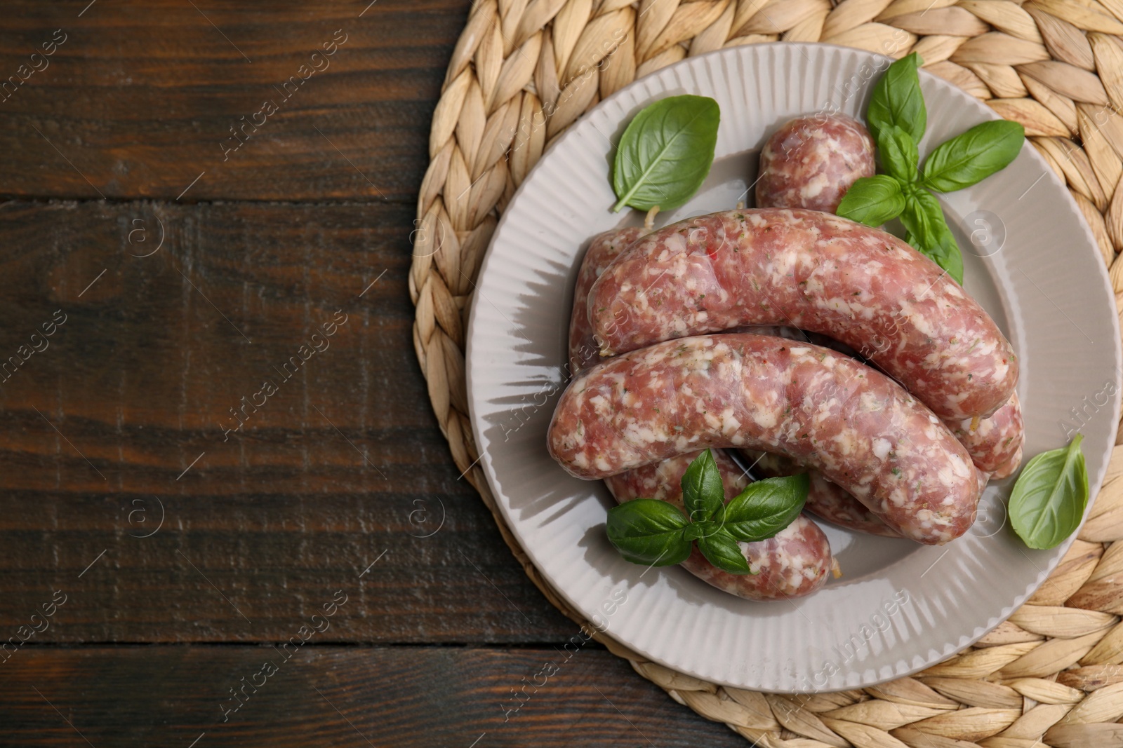 Photo of Raw homemade sausages and basil leaves on wooden table, top view. Space for text
